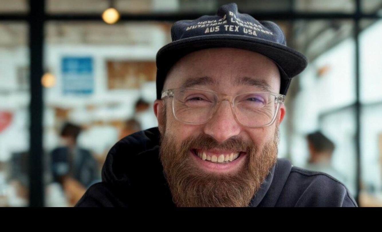 Portrait of Todd Larsen, smiling, in a cap and hoodie